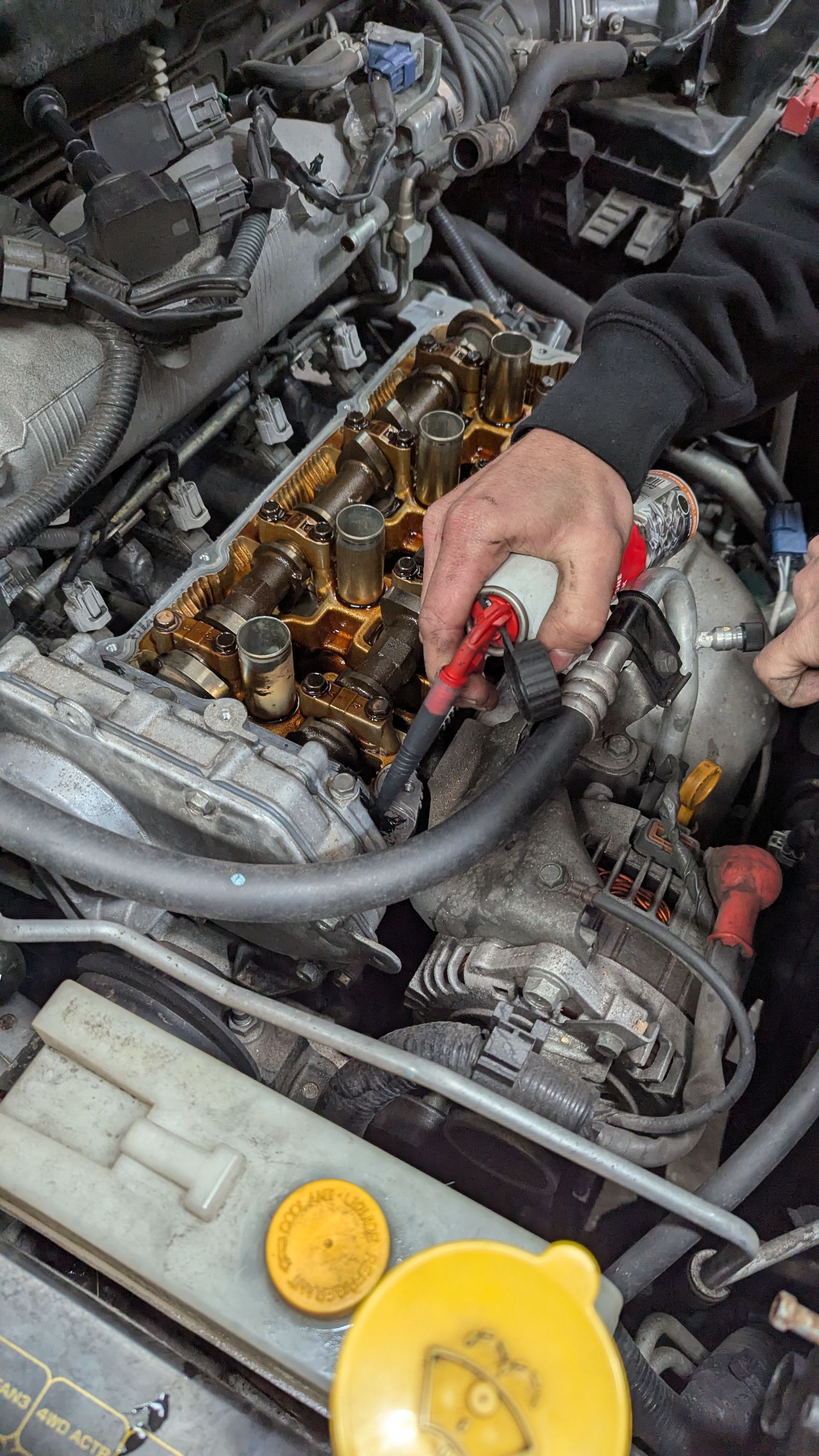Person working on a car engine; spraying cleaner. Engine components visible. Yellow and brown tones  — ATD Automotive in North Wollongong, NSW