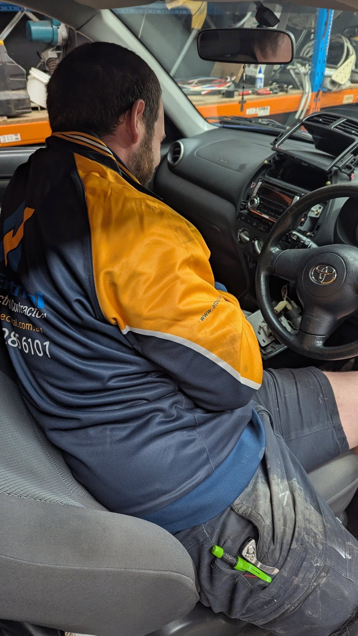 Man Seated in A Car, Wearing a Blue and Gold Jacket, with A Screwdriver in Pocket — ATD Automotive in North Wollongong, NSW