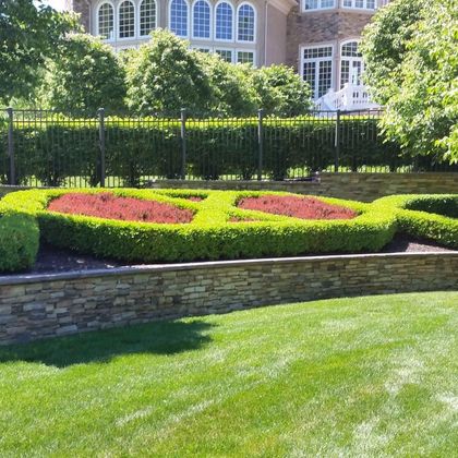 A lush green lawn with a stone wall and a house in the background