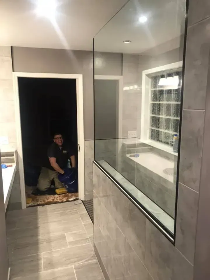 A man is kneeling in a bathroom next to a window.