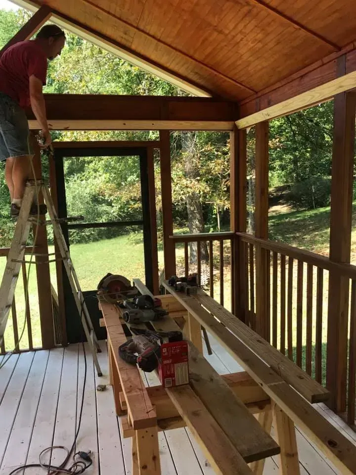 A man is standing on a ladder in a screened in porch.
