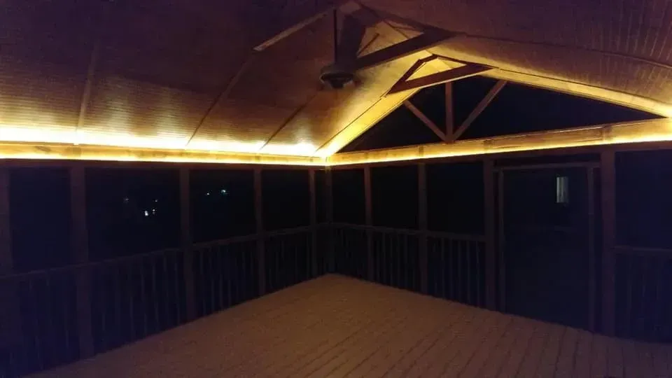 A screened in porch with lights on the ceiling at night.