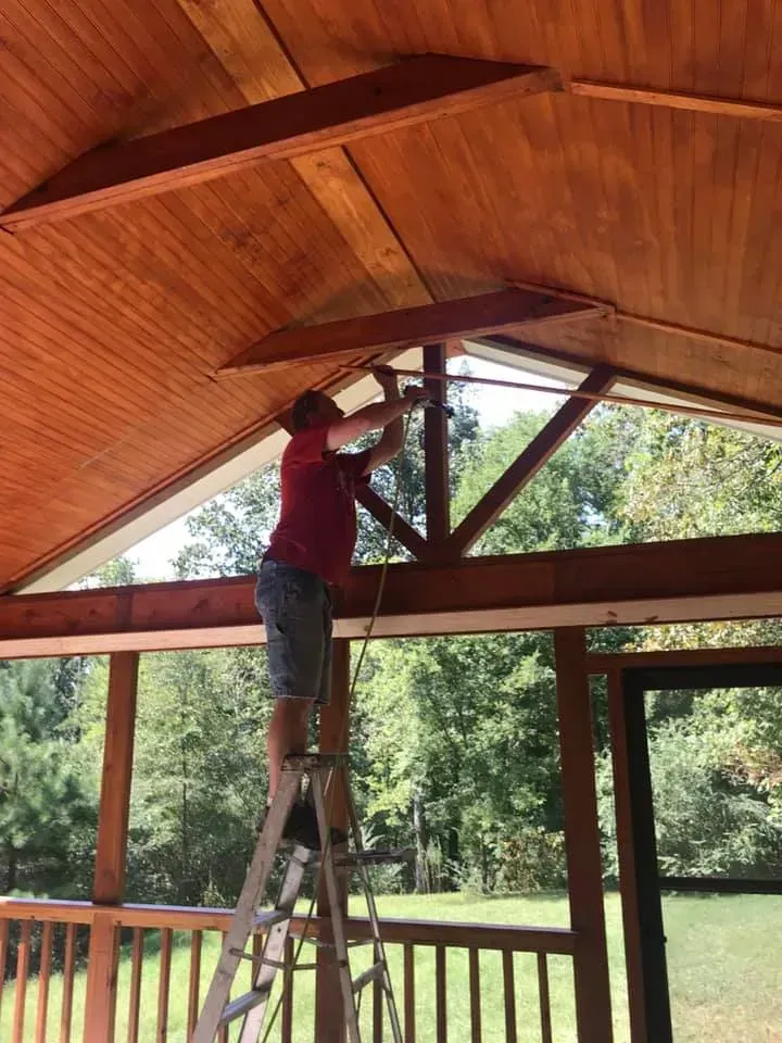 A man is standing on a ladder working on a wooden ceiling.