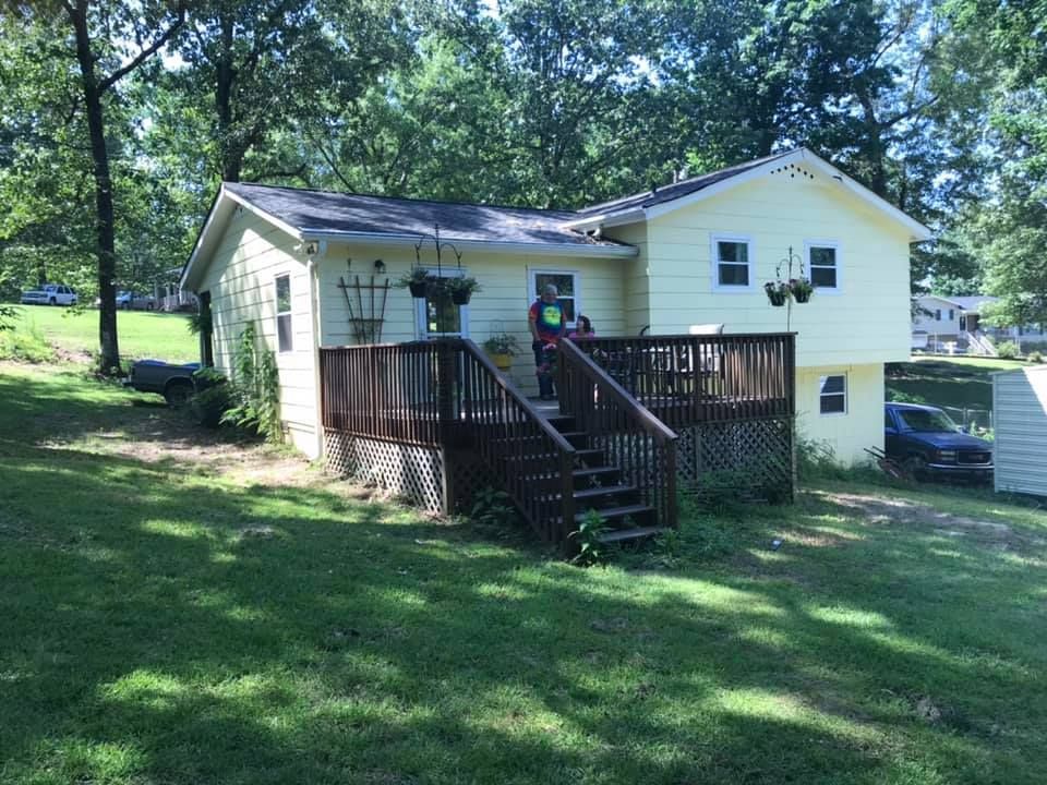 A small yellow house with a wooden deck and stairs.