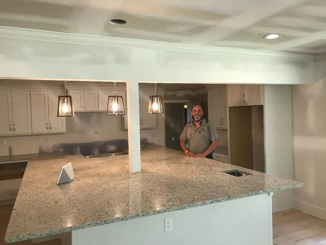A man is standing in a kitchen with a granite counter top.