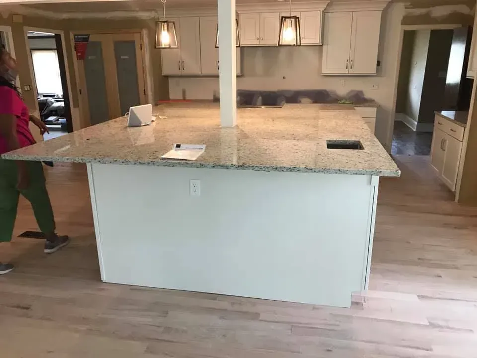 A woman is standing in a kitchen with a large island in the middle.