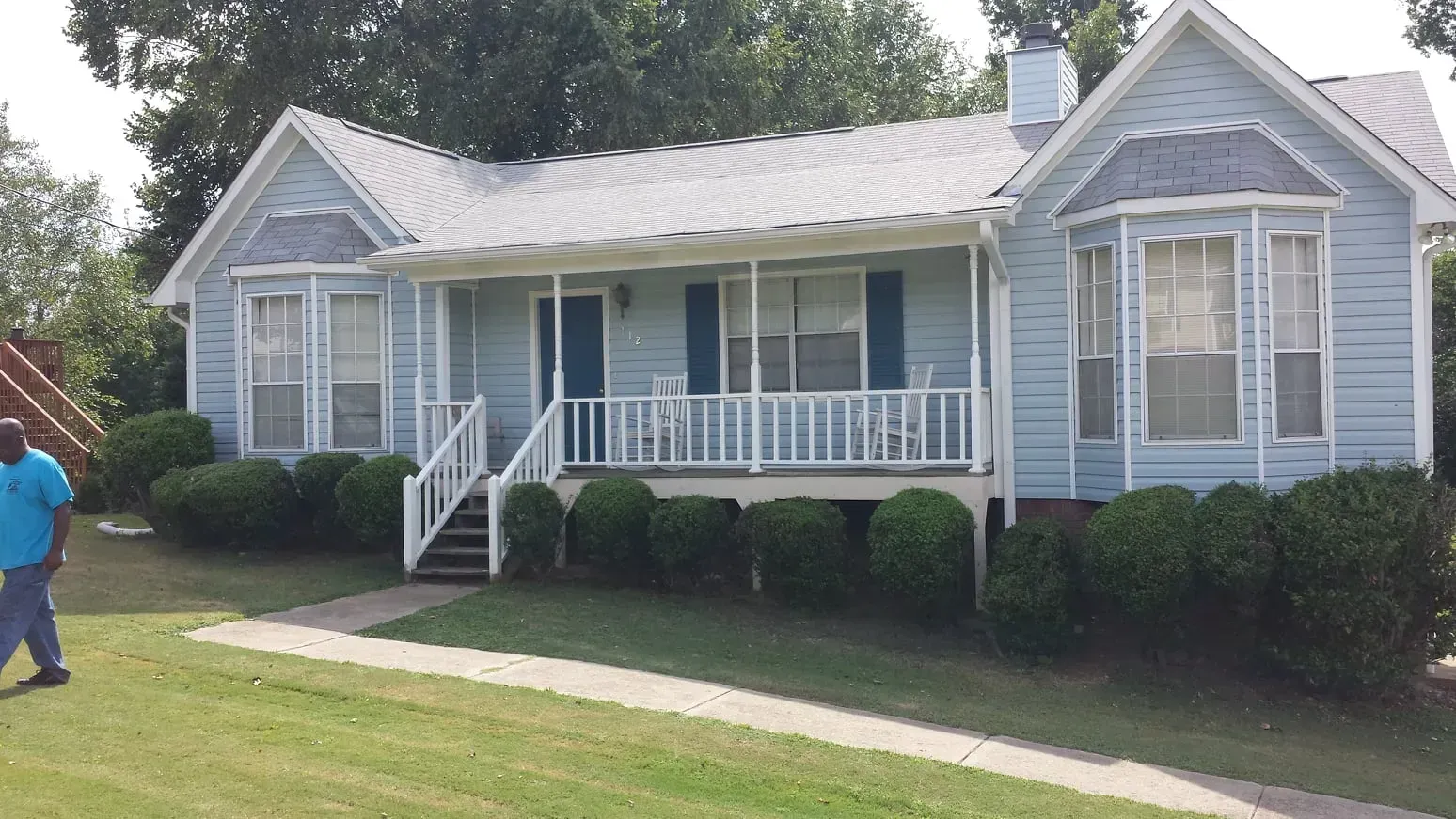 A man in a blue shirt is standing in front of a blue house