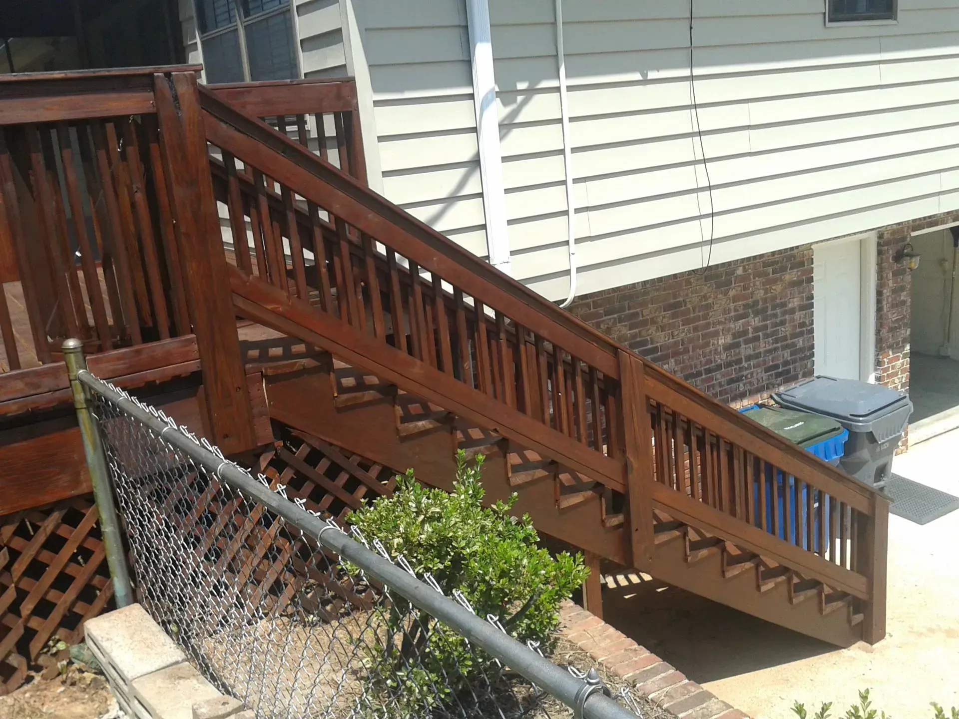 A wooden deck with stairs leading up to a house behind a chain link fence.