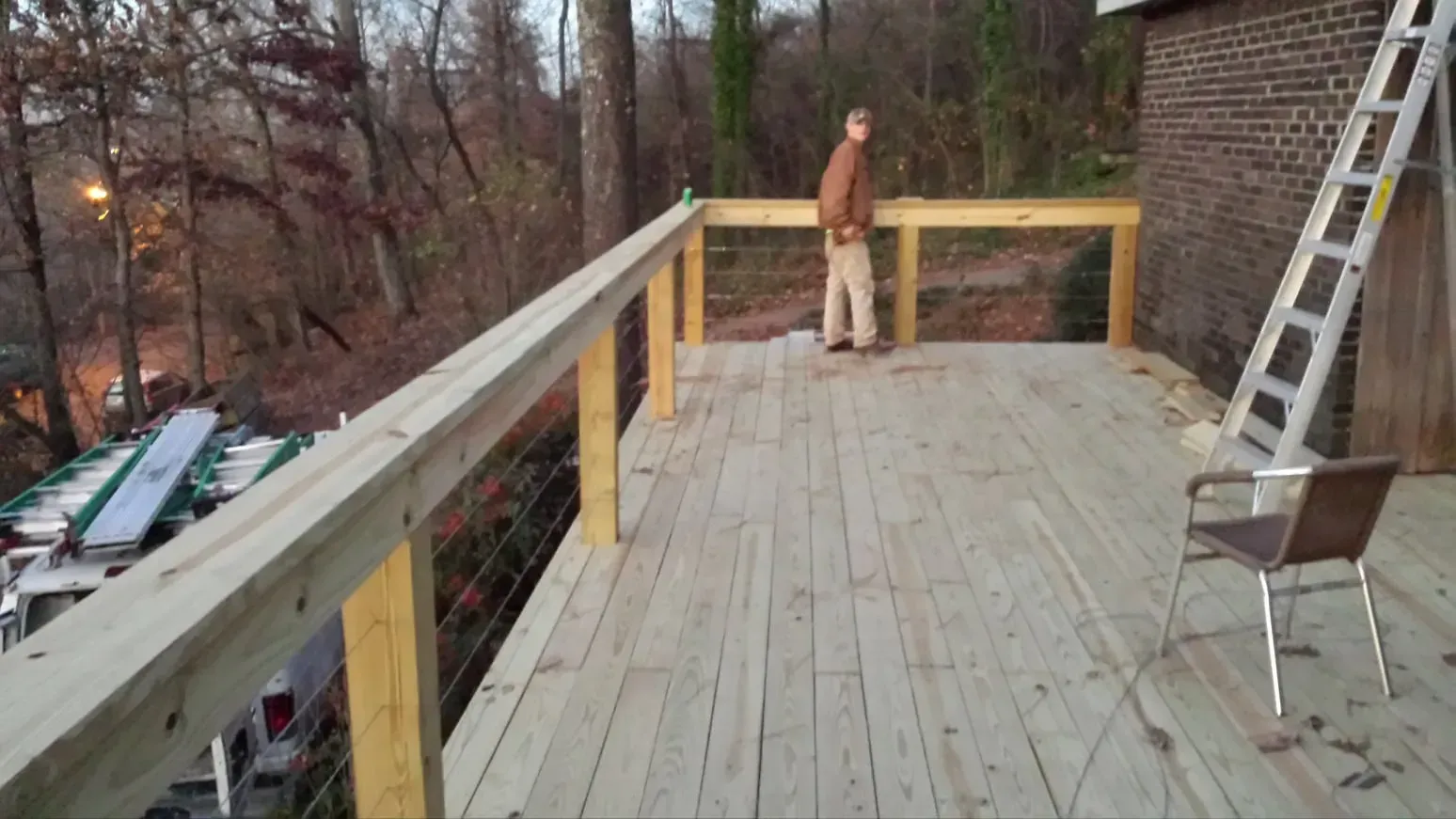 A man is standing on a wooden deck overlooking a forest.