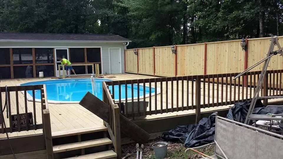 A swimming pool is surrounded by a wooden deck and fence.