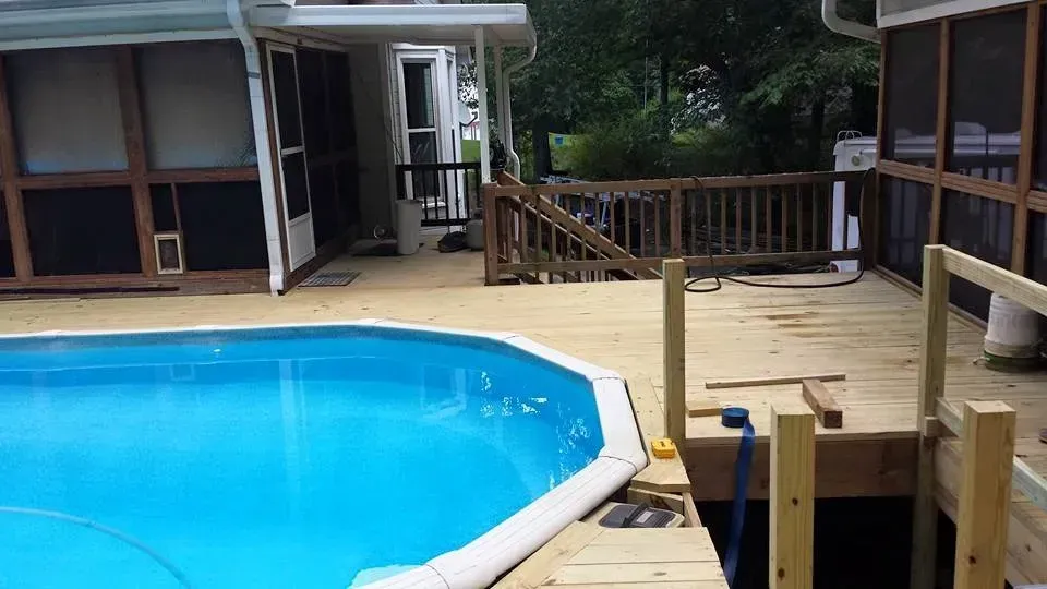 A swimming pool is surrounded by a wooden deck and screened in porch.