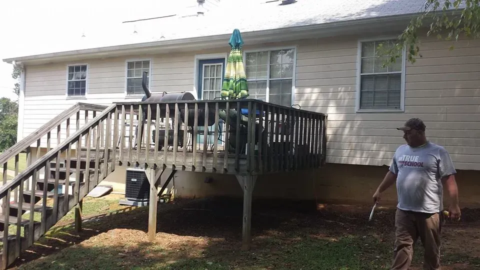 A man is standing in front of a house with a deck and stairs.