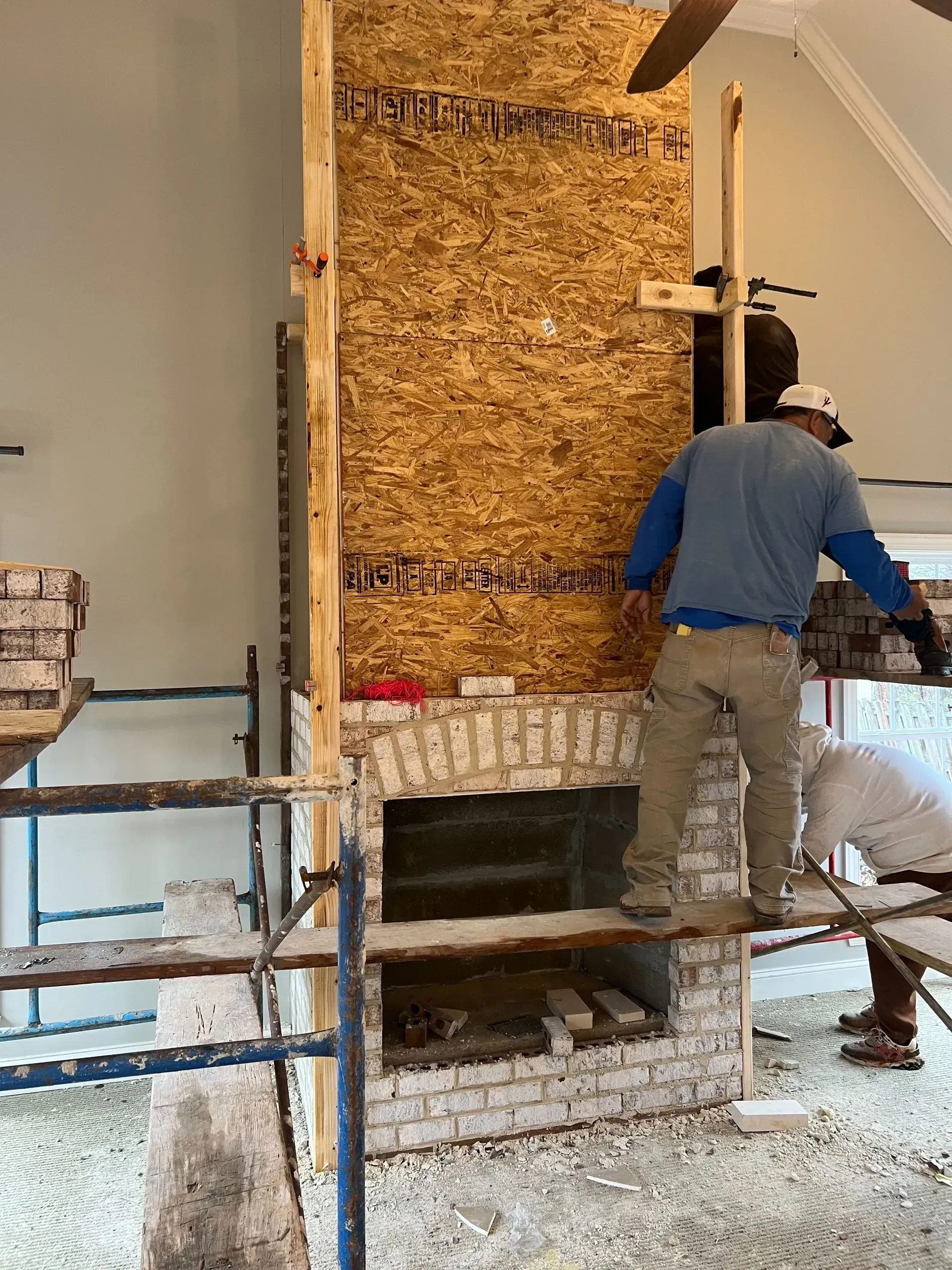 Two men are working on a fireplace in a living room.