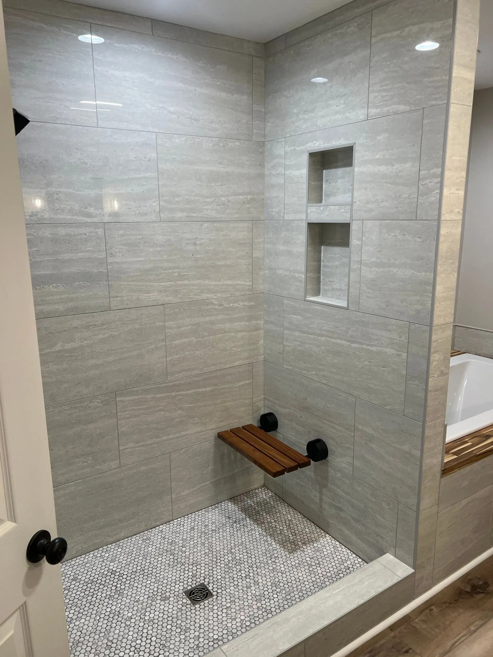 A bathroom with a walk in shower with a wooden seat.