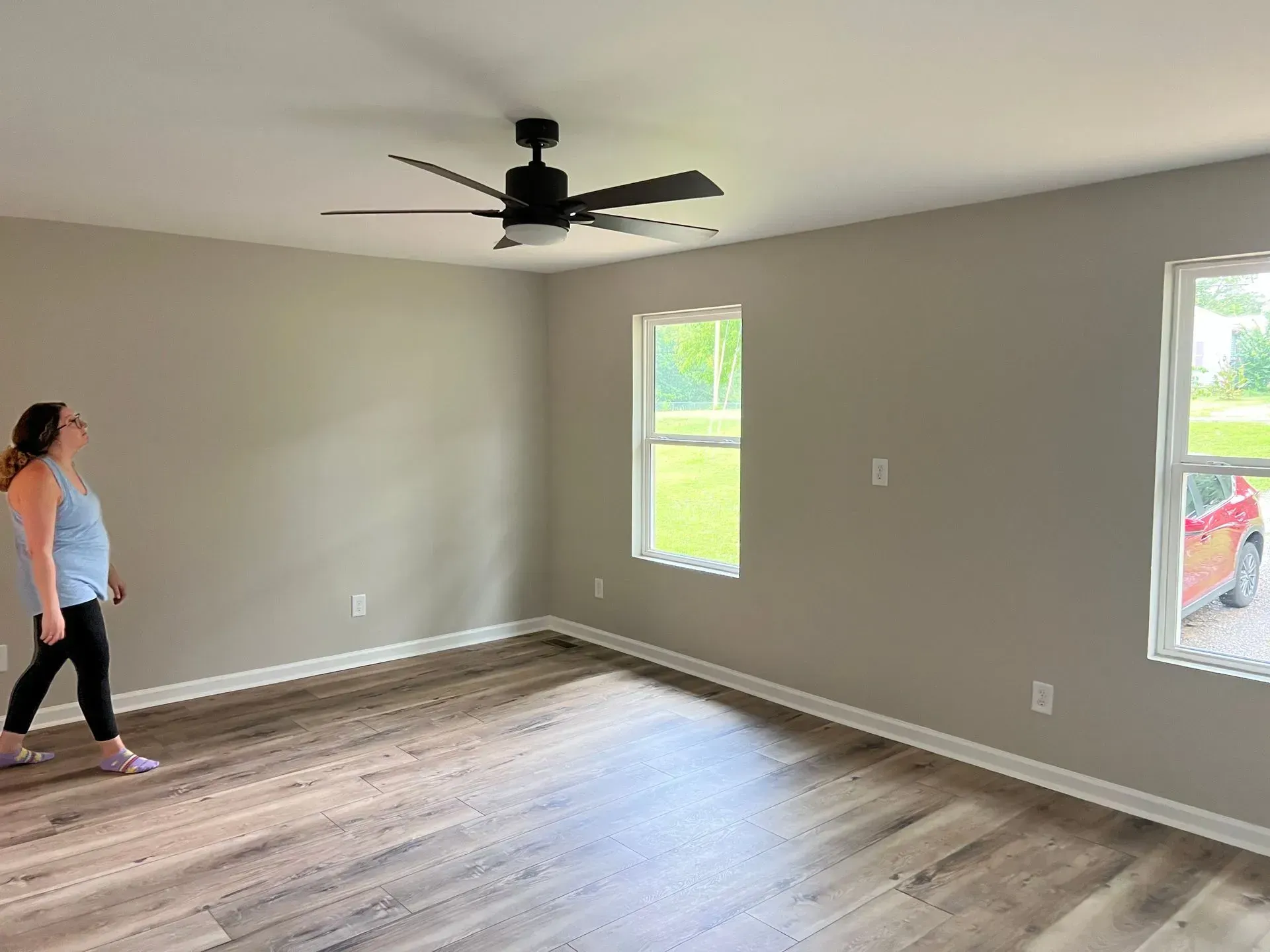 A woman is standing in an empty room with a ceiling fan.