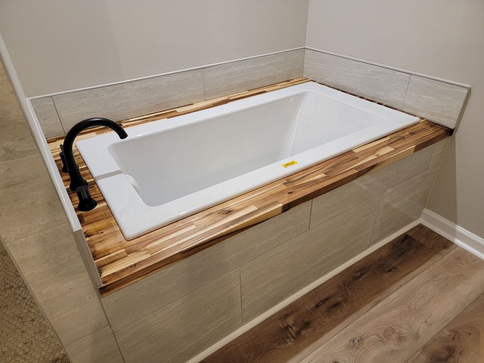 A bathtub with a wooden counter top in a bathroom.