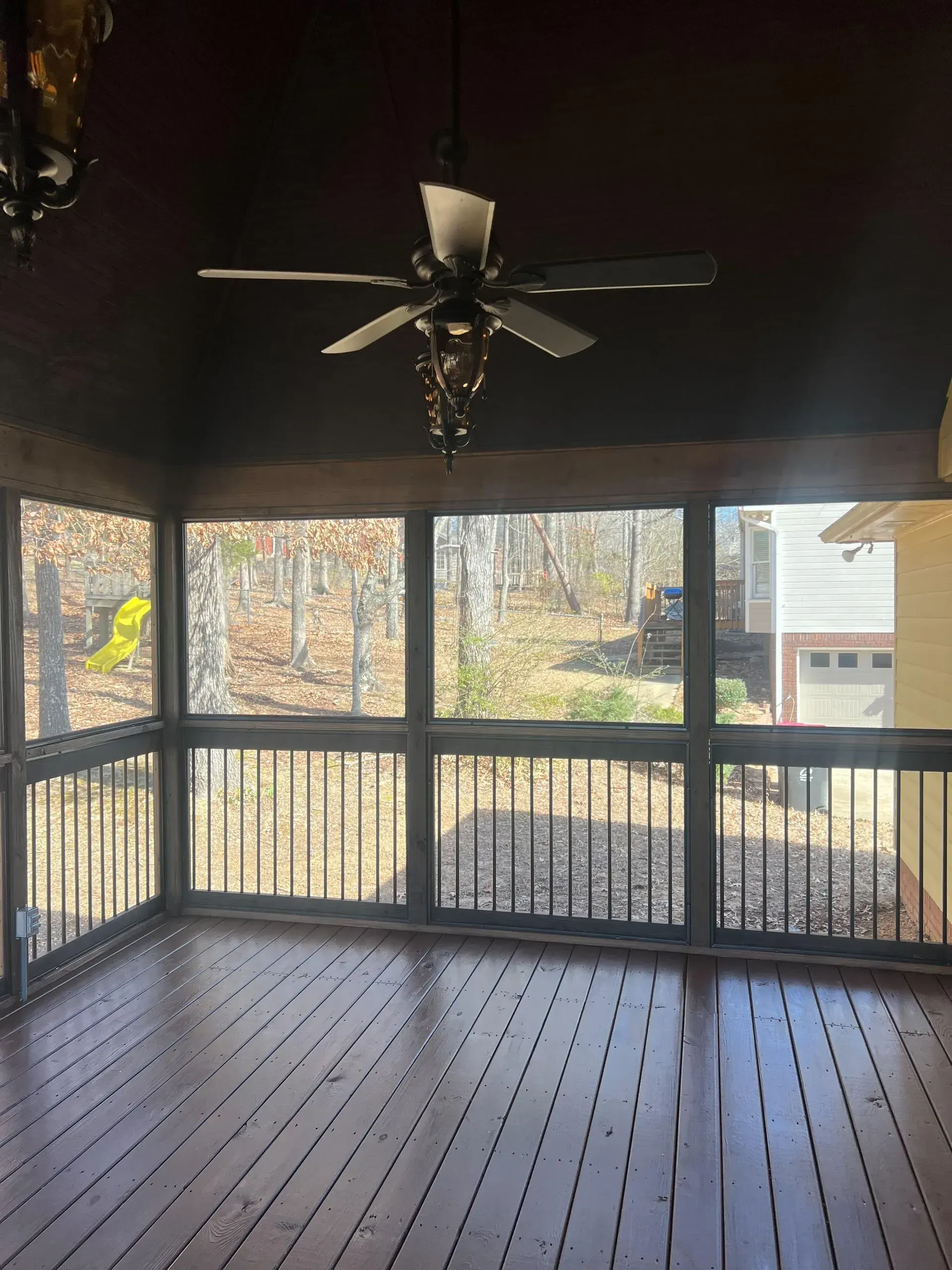 An empty screened in porch with a ceiling fan