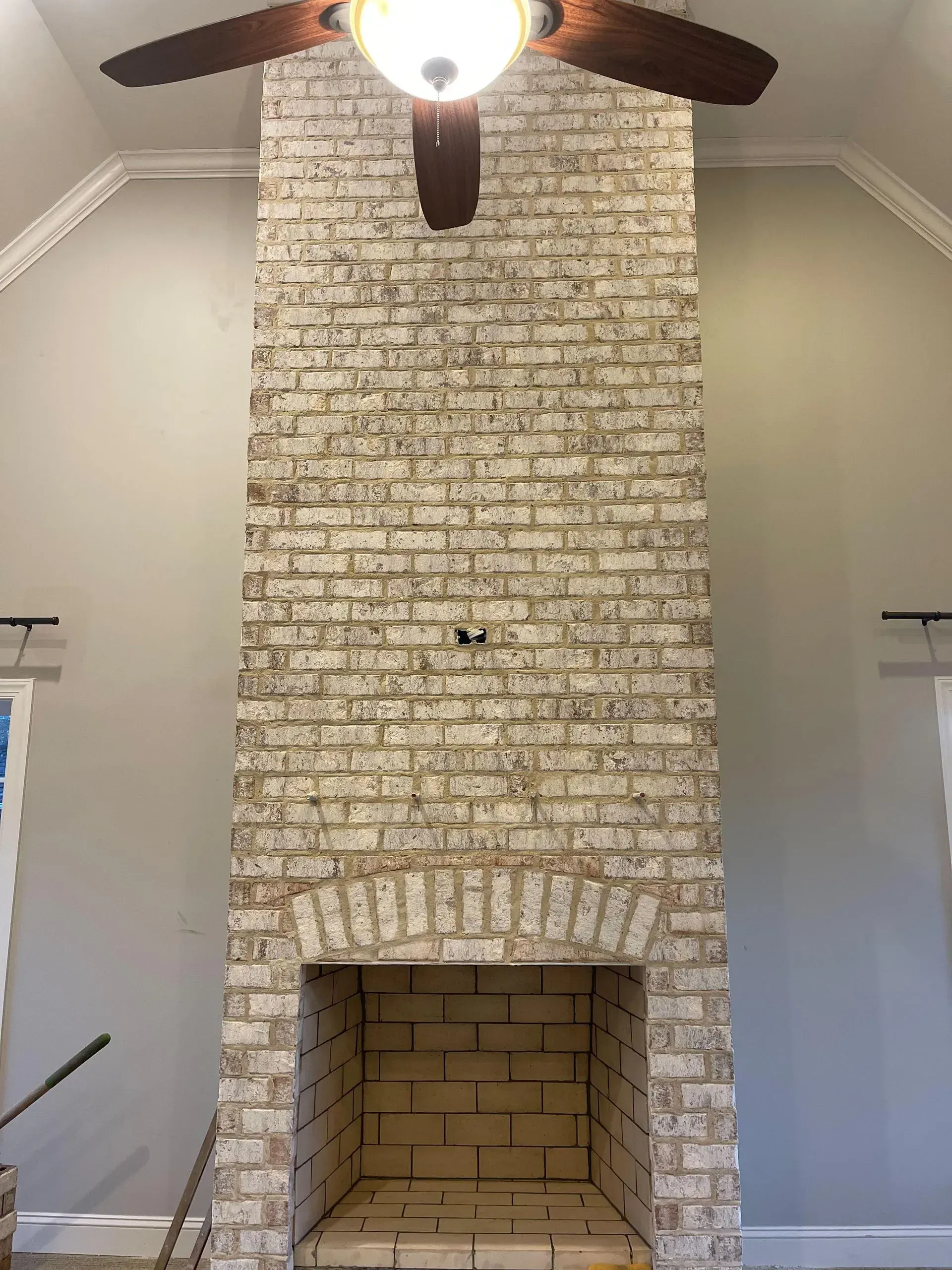 A brick fireplace with a ceiling fan in a living room.