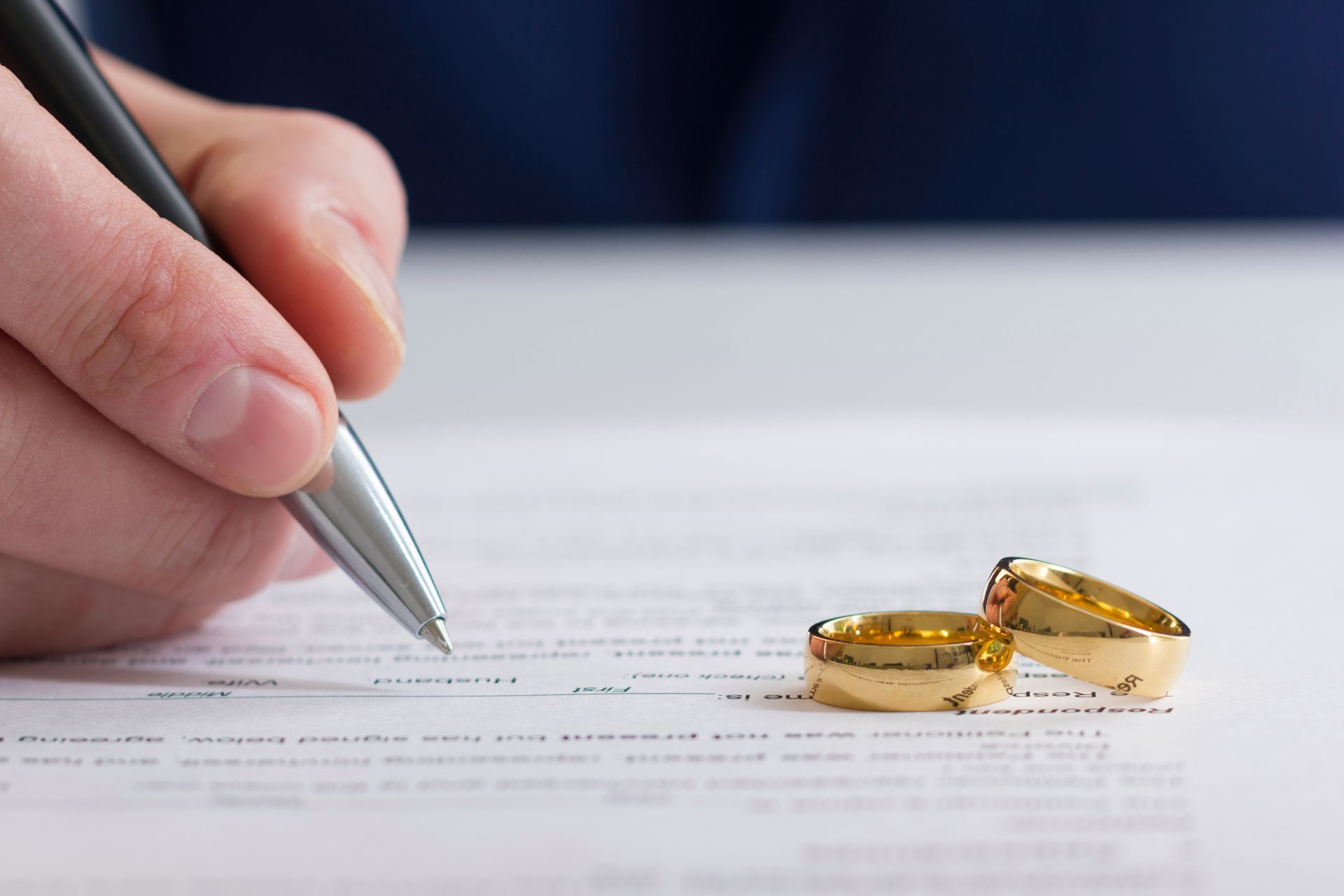 A person is writing on a piece of paper with two wedding rings on it.