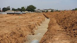 Excavated trench lined with gravel running through a dry dirt construction site