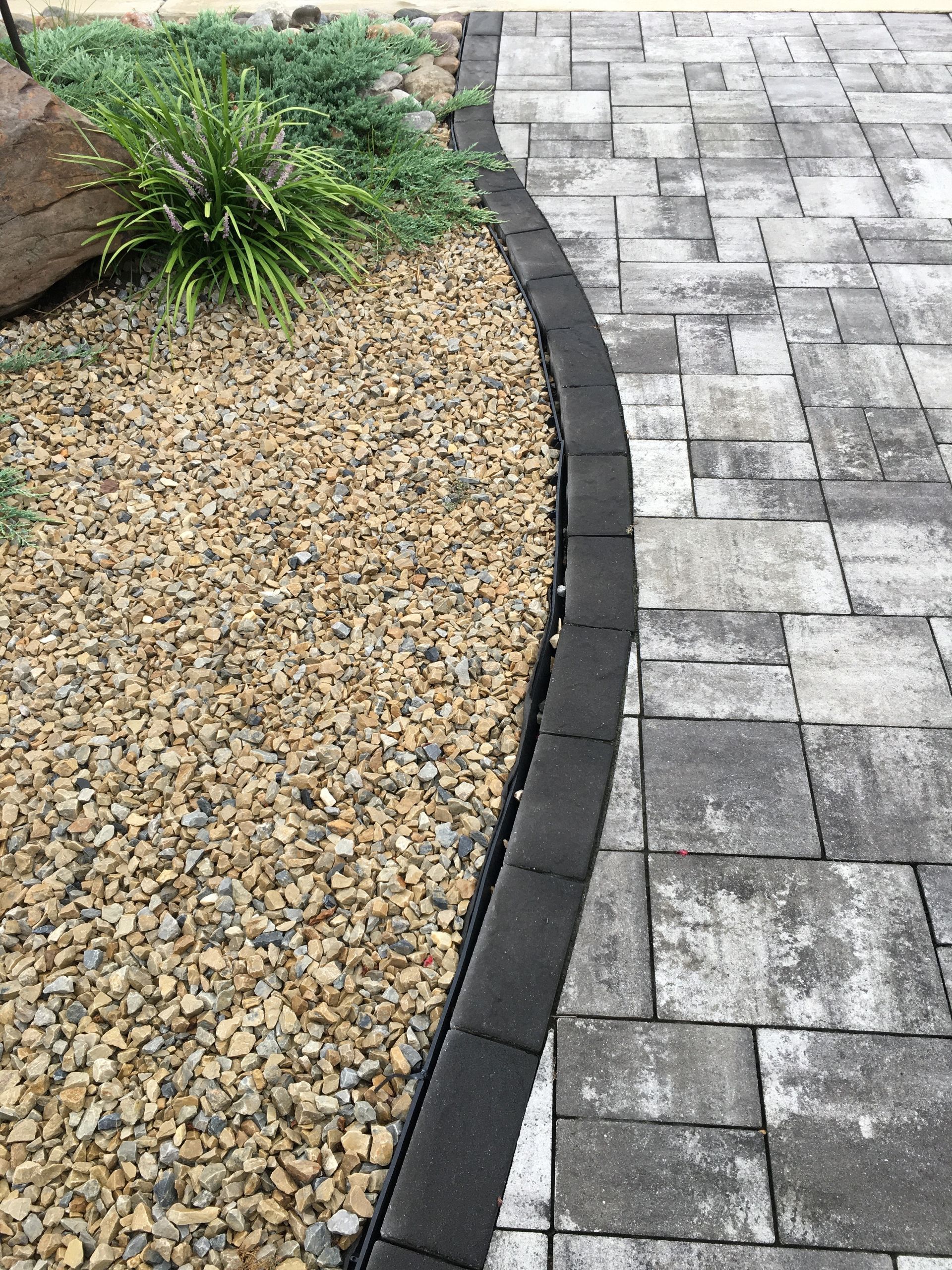 Curved border between gravel bed and gray paver walkway in a landscaped yard