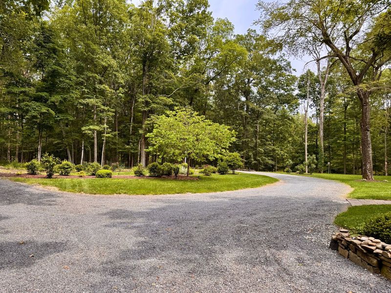 Gravel driveway curving through a green wooded park with trees and a stone border