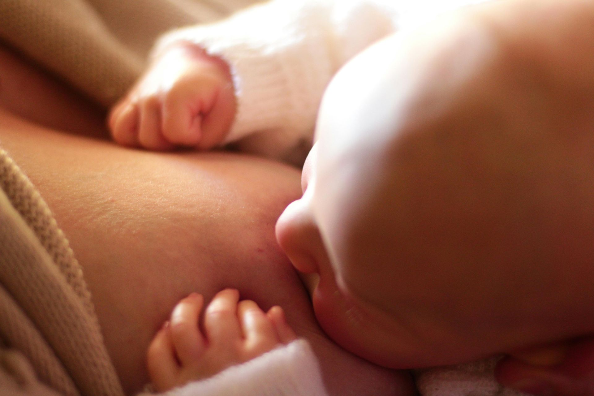 Baby breastfeeding, close-up. Baby's face and hands visible, grasping clothing. Soft, warm lighting.