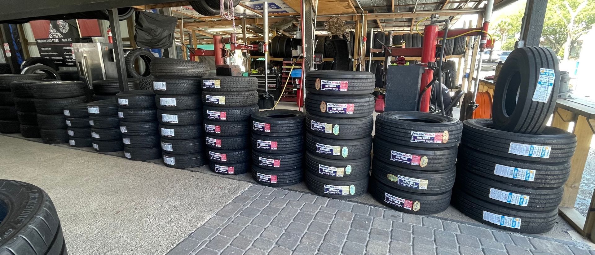 Stacks of black racing tires in a garage, with a forklift and workshop equipment in the background