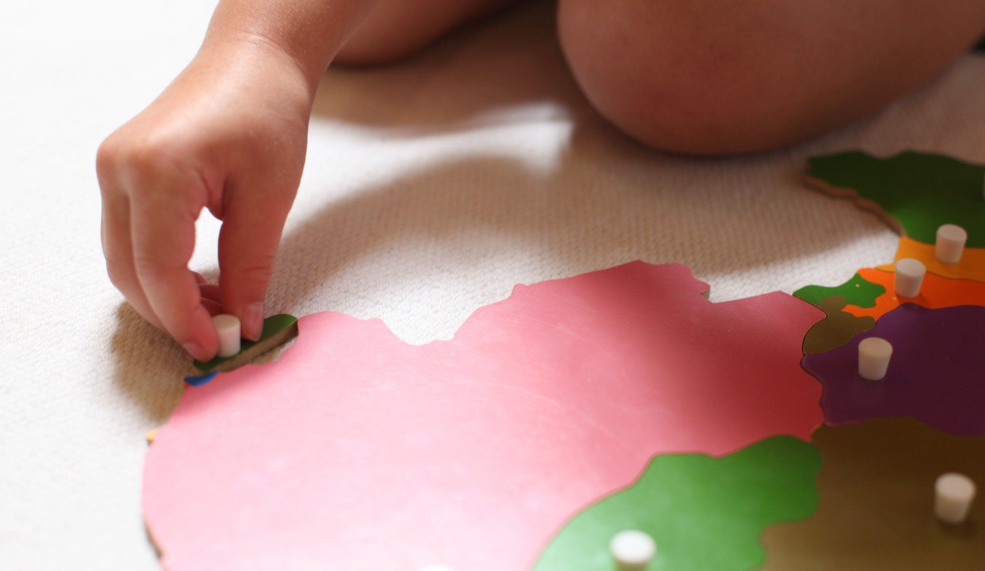 Child's hand placing a white peg on a pink wooden puzzle map. Close-up.