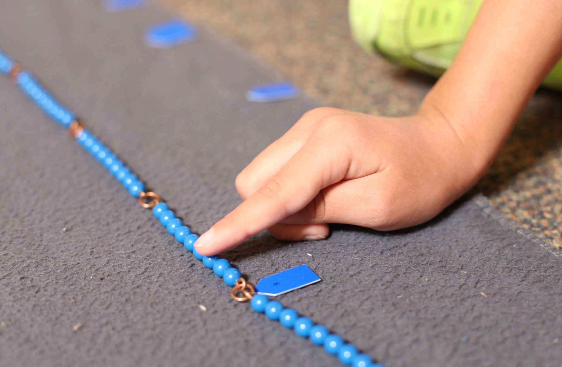 Child's hand pointing at blue beads on a line, used for counting or math.