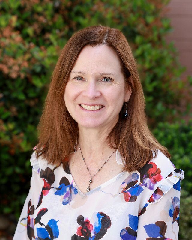 A woman wearing a green shirt and a black sweater is smiling for the camera.