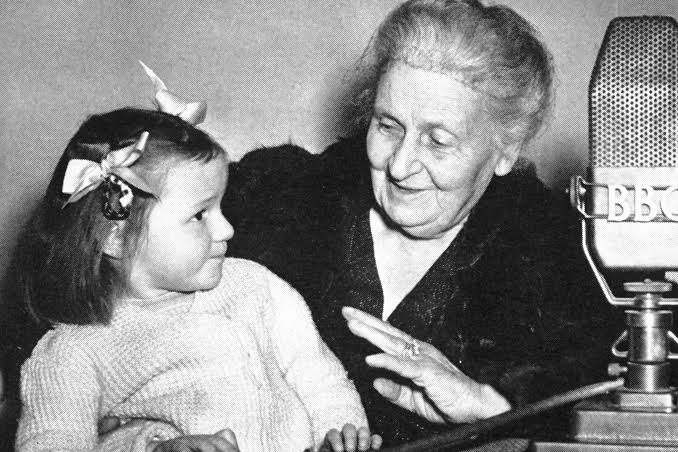 Maria Montessori and a young girl at a BBC microphone, both smiling, possibly recording.