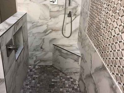 A walk in shower with marble tiles and a bench.