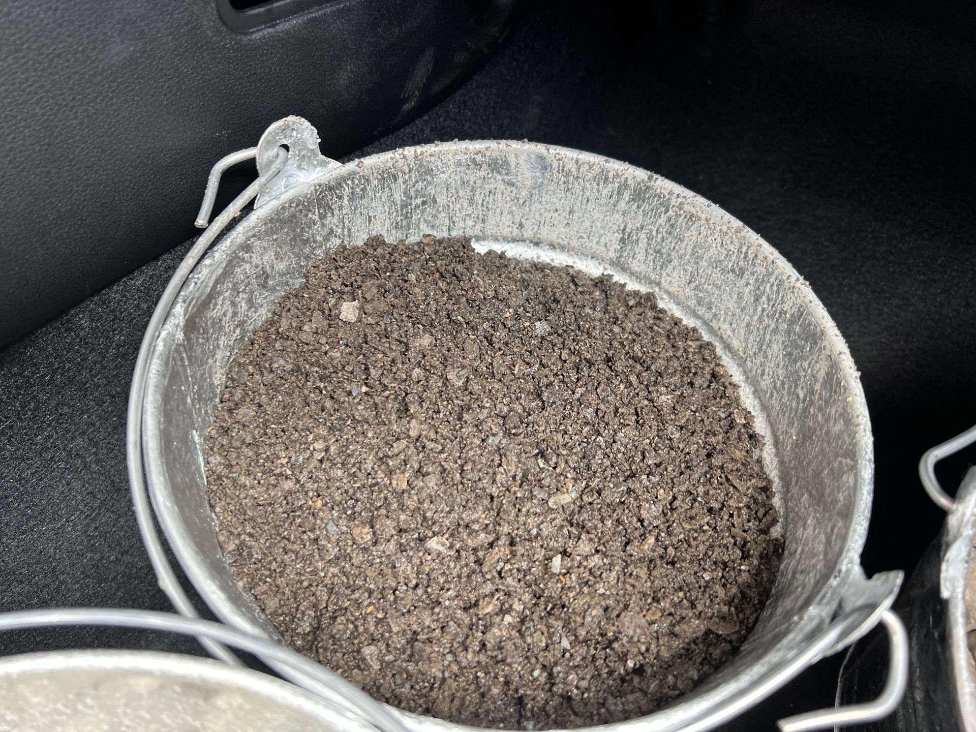 A metal bucket filled with dirt is sitting on the trunk of a car.