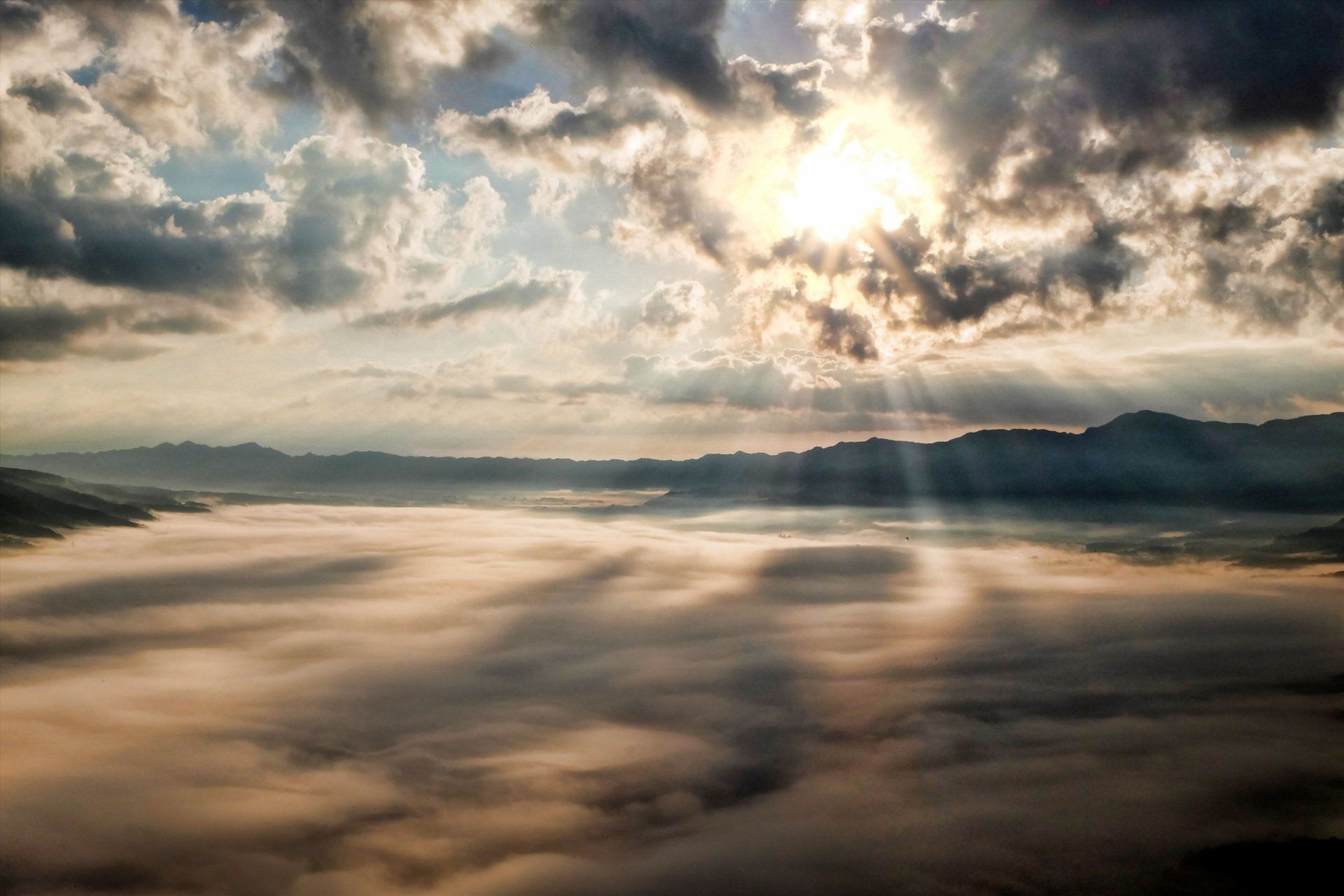 Sunrise over a sea of clouds with sunbeams and distant mountains