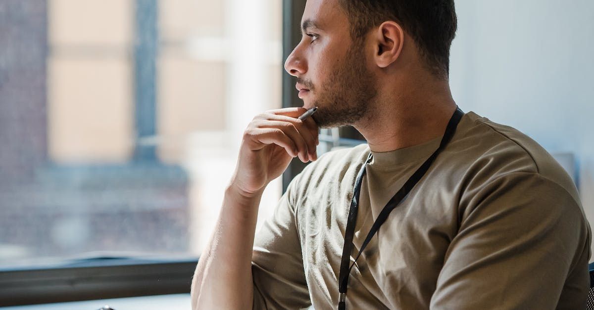 Man sitting by a window, looking outside thoughtfully with his hand on his chin.