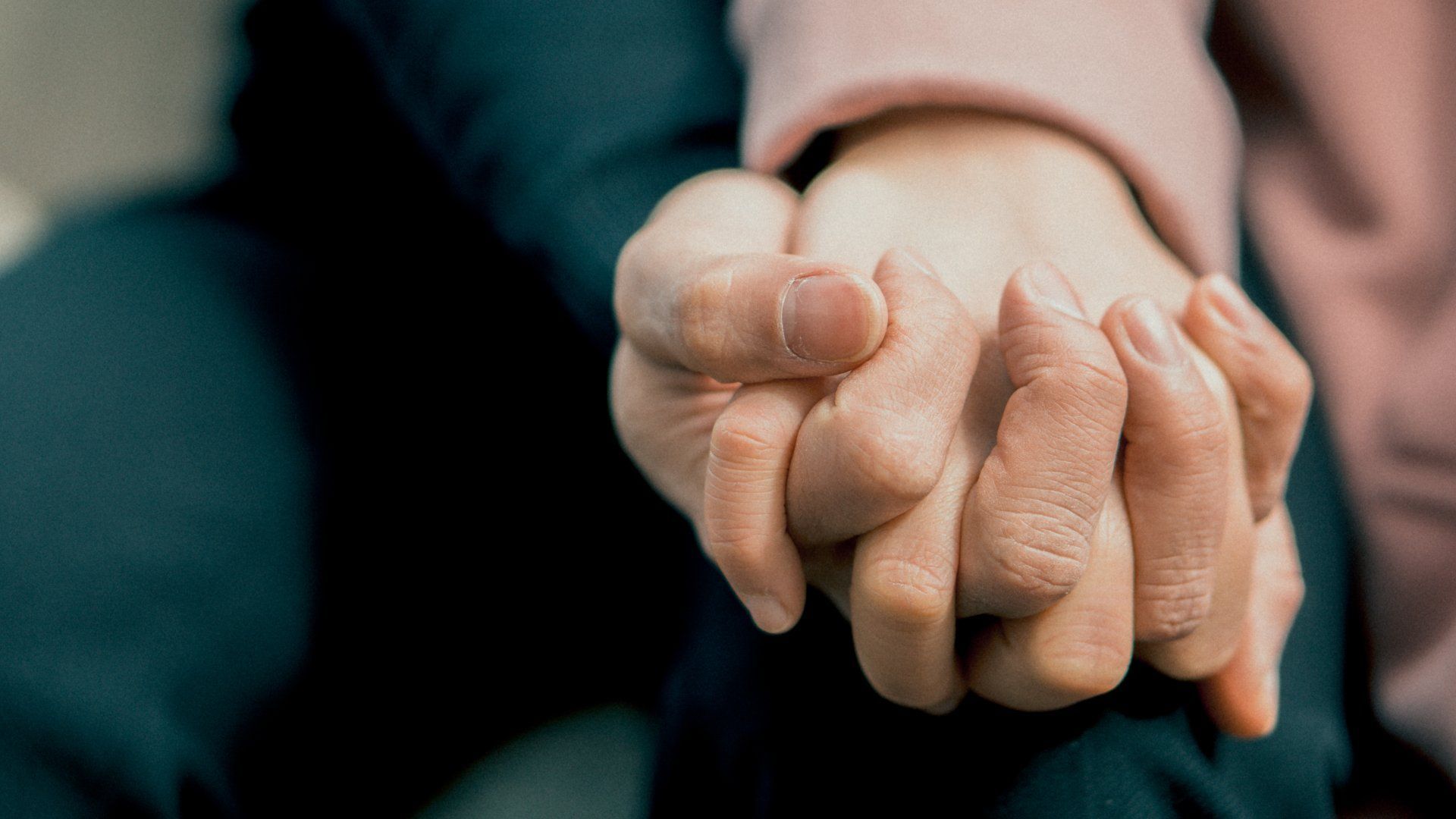 Two hands clasped together in a supportive hold, with a blurred dark background.