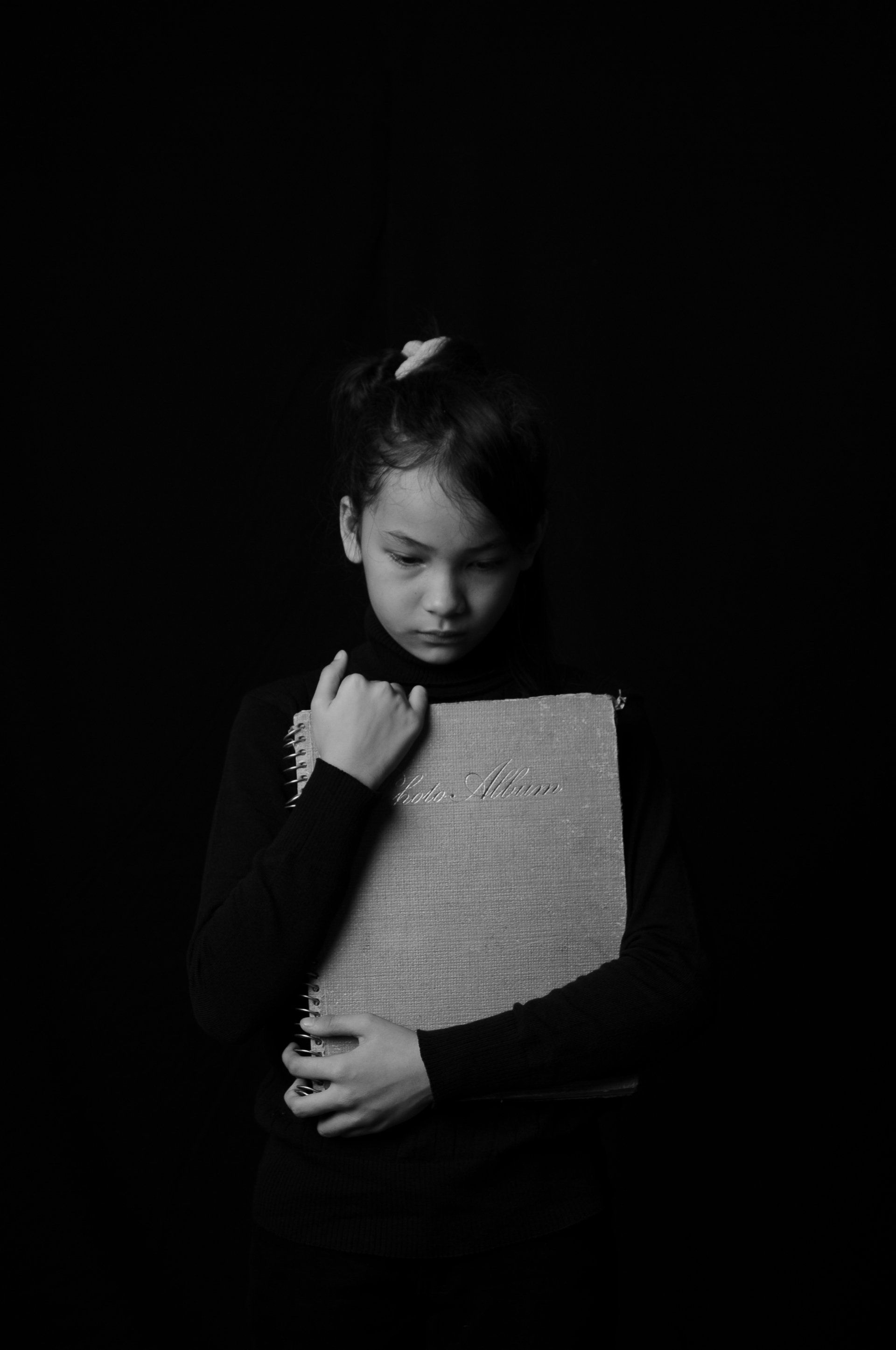 Person in dark clothing holding a textured board against a black background, looking down.