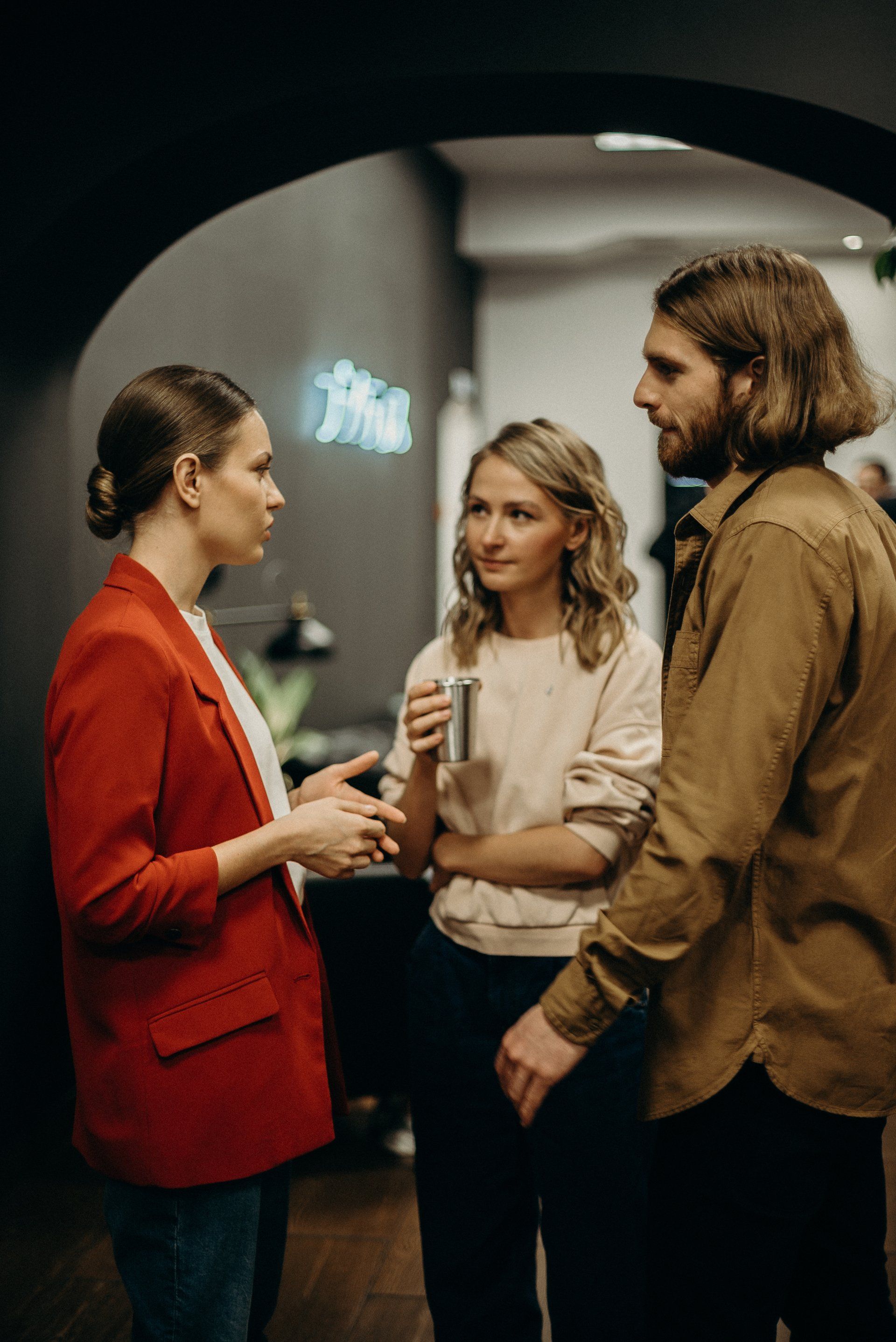 Three people talking at a cocktail event, one holding a drink in a dimly lit room.