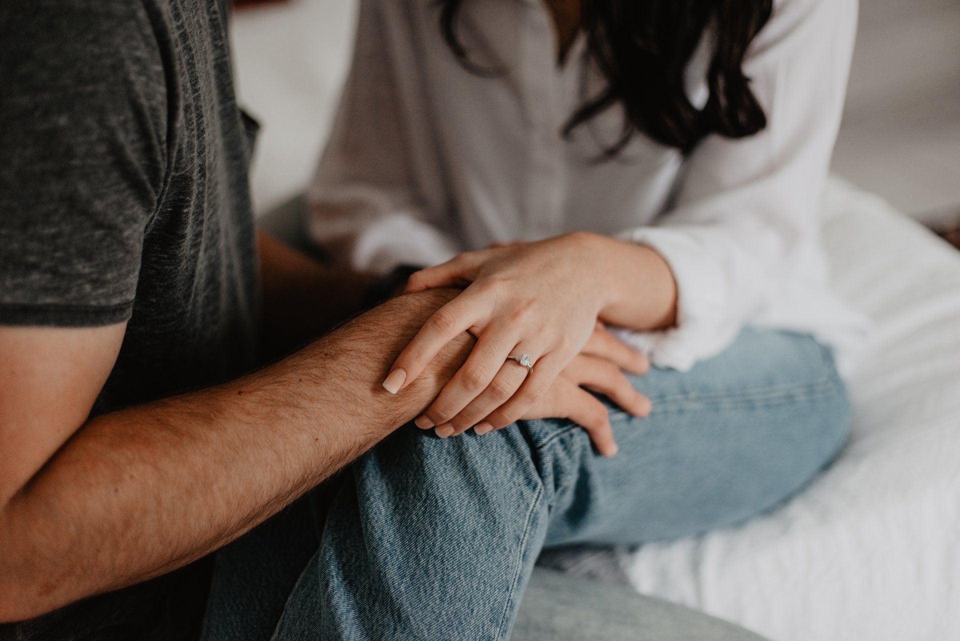 Two people sitting close together, holding hands on a bed