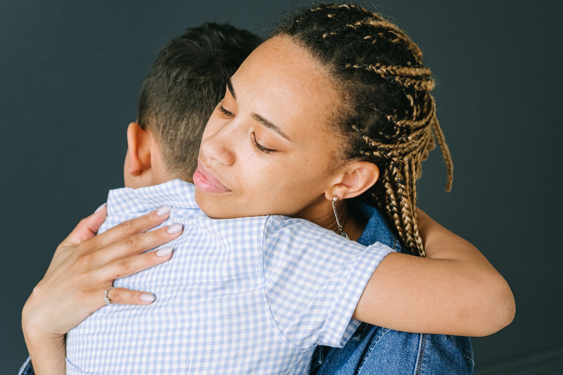Two people embracing warmly against a dark background, eyes closed in a comforting hug.