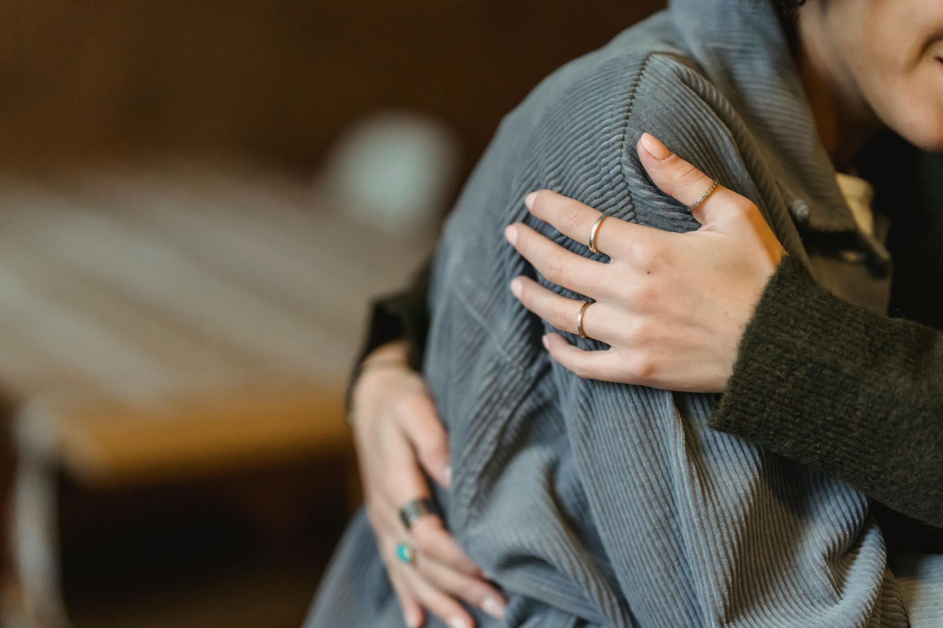 Two people hugging, one hand with a ring on a gray sweater shoulder