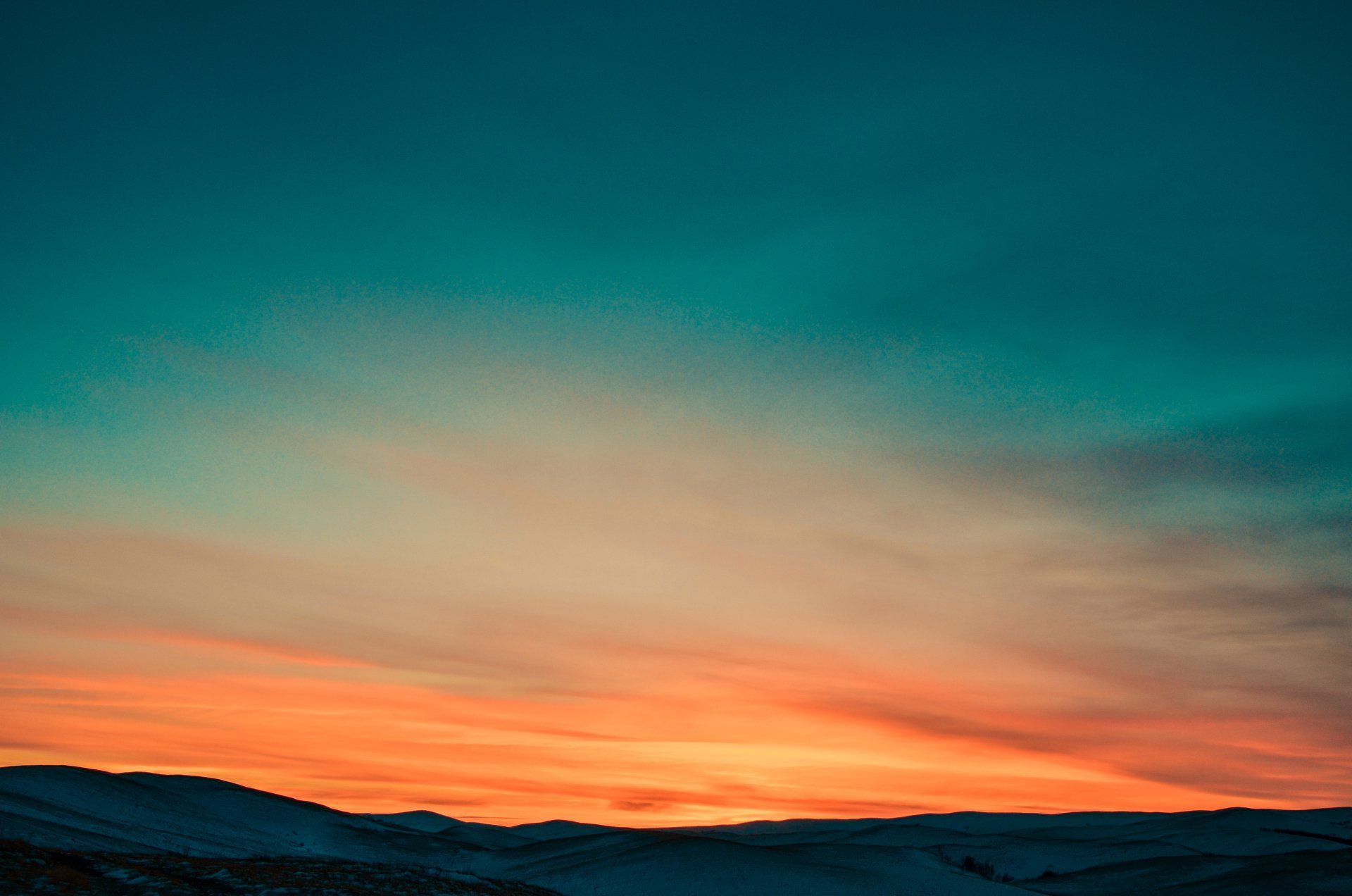 Colorful sunset over dark hills, with orange and teal sky fading into dusk.