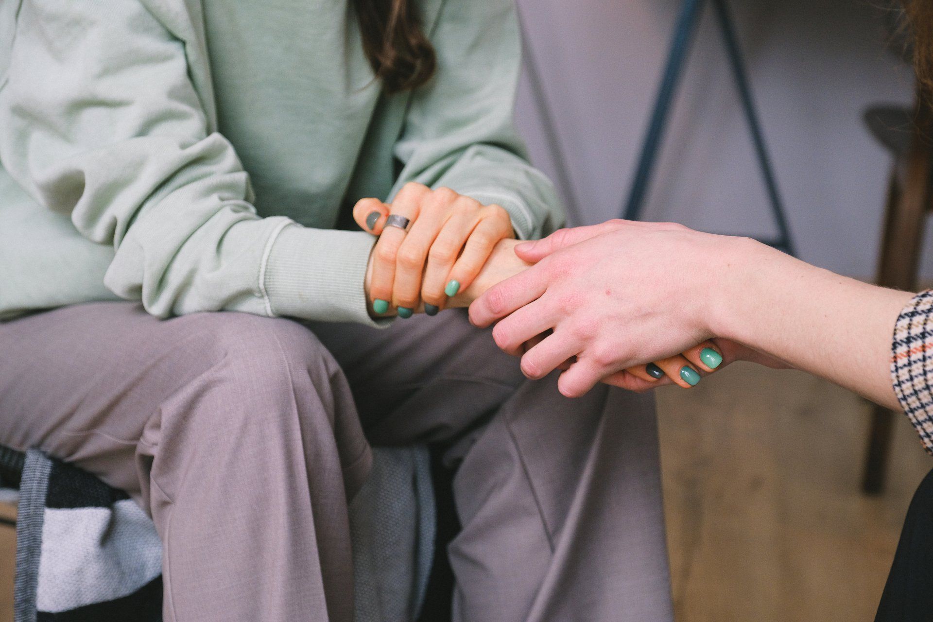 Two people holding hands, one in a mint sweater and gray pants, seated indoors.