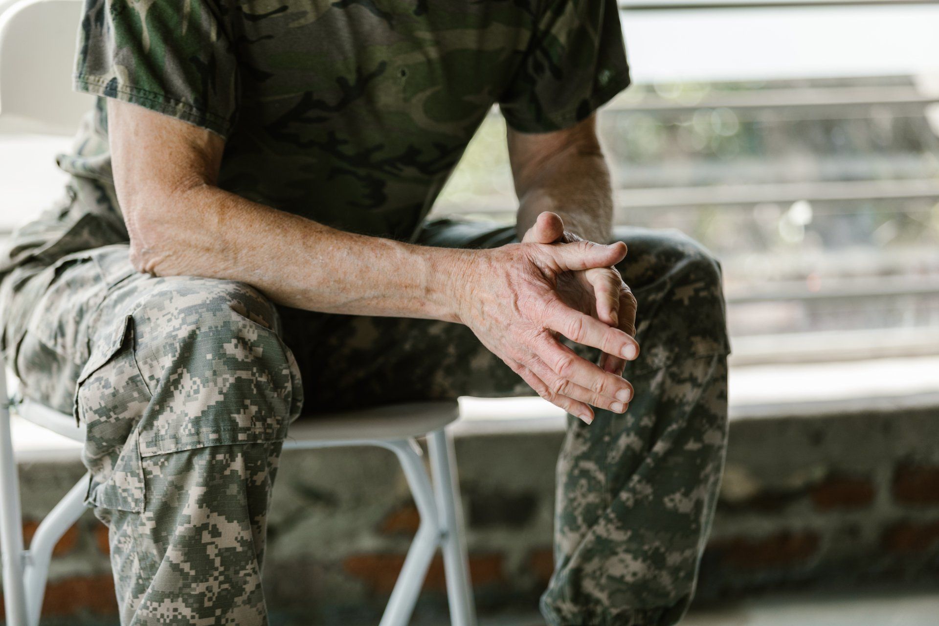 Soldier in camouflage sitting with clasped hands on a bench outdoors