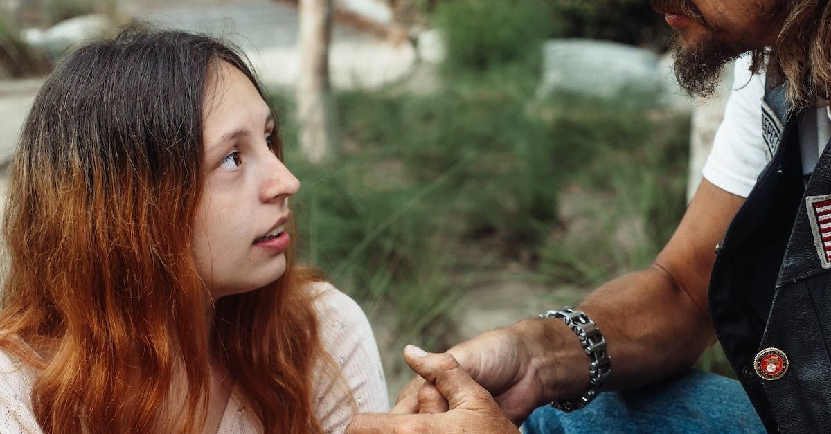Two people talking outdoors, one seated and looking up at the other gesturing nearby