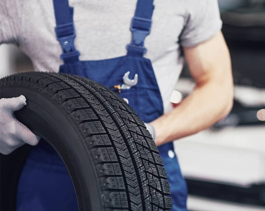 A man in blue overalls is holding a tire in his hands.