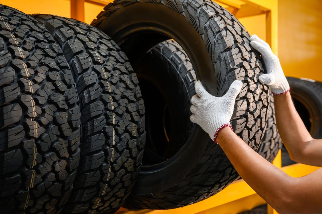 A person is holding a tire in front of a stack of tires.