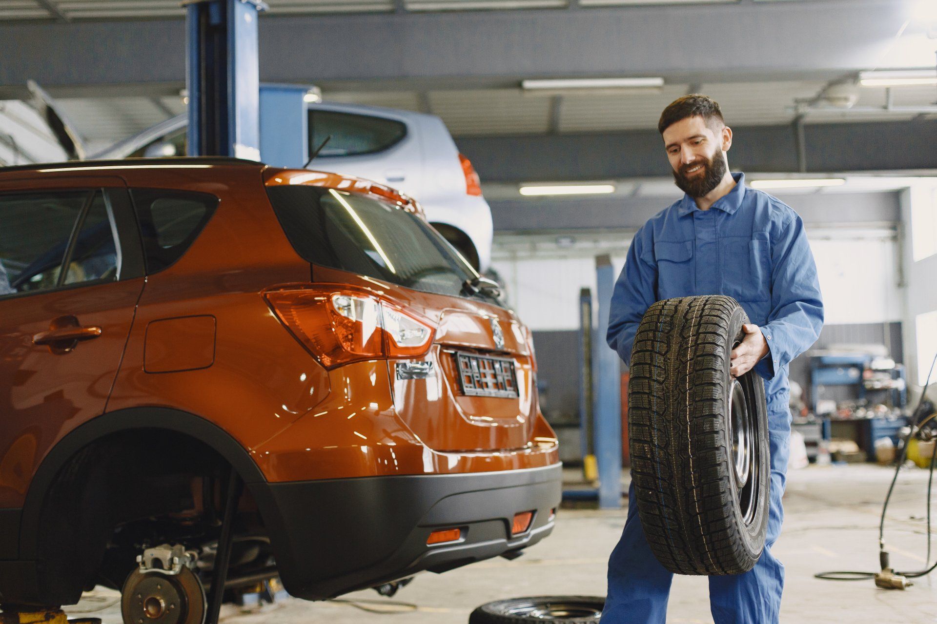 A man is holding a tire in front of a car in a garage.