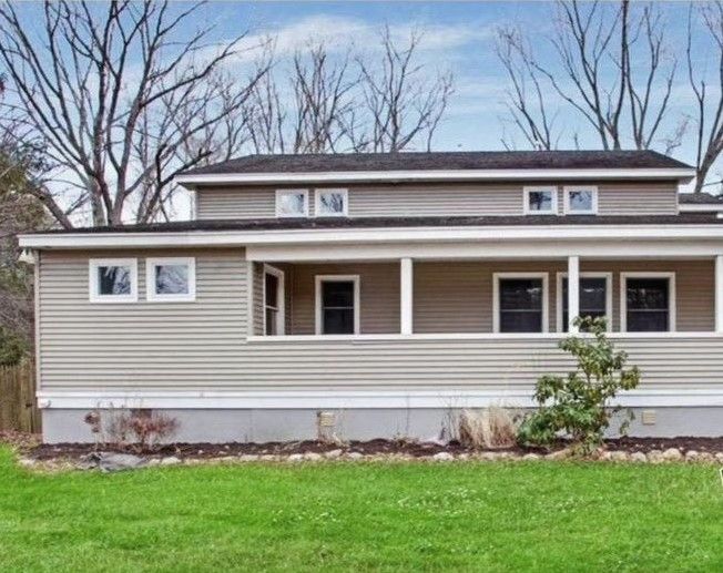 A house with a porch and a lot of windows is sitting on top of a lush green field.